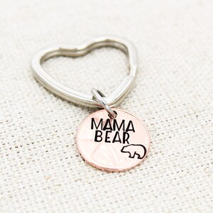 May include: A copper-colored key chain with a heart-shaped ring and a round charm that says "Mama Bear" with a small bear silhouette.
