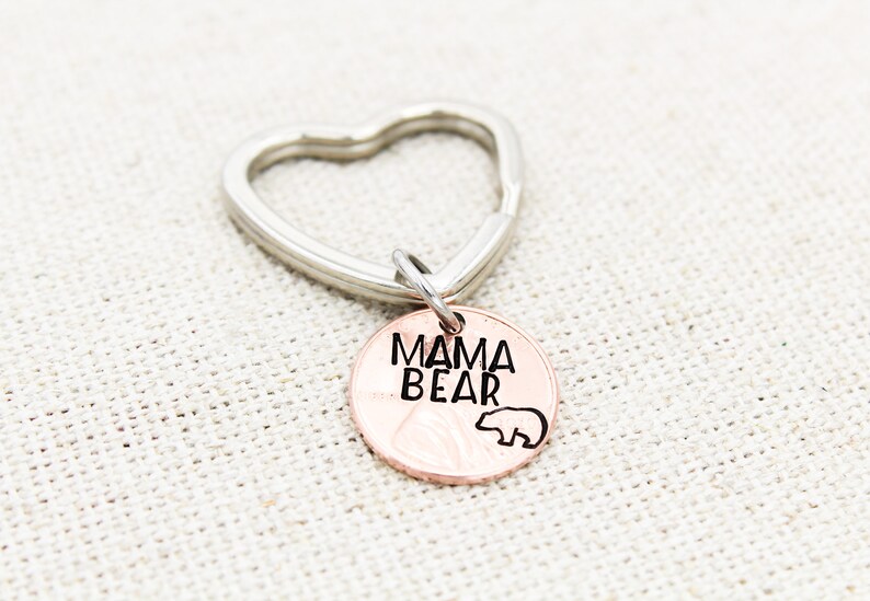 May include: A copper-colored key chain with a heart-shaped ring and a round charm that says "Mama Bear" with a small bear silhouette.