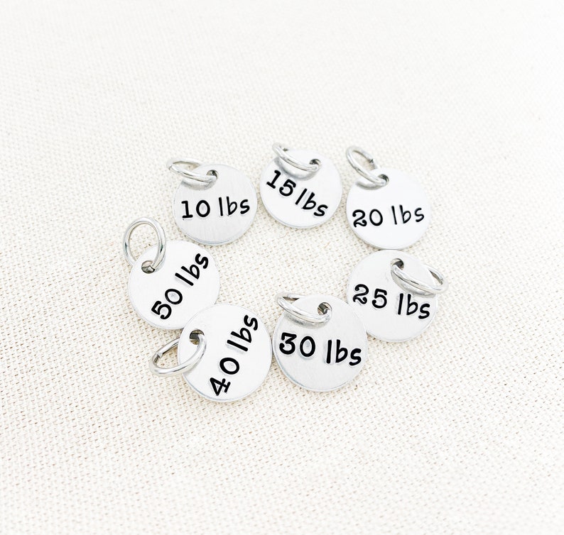 May include: Silver weight charms with different weight measurements in pounds, including 10 lbs, 15 lbs, 20 lbs, 25 lbs, 30 lbs, 40 lbs, and 50 lbs.
