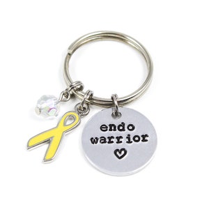 May include: Silver keychain with a yellow ribbon charm, a crystal charm, and a round silver charm with the text "endo warrior" and a heart.