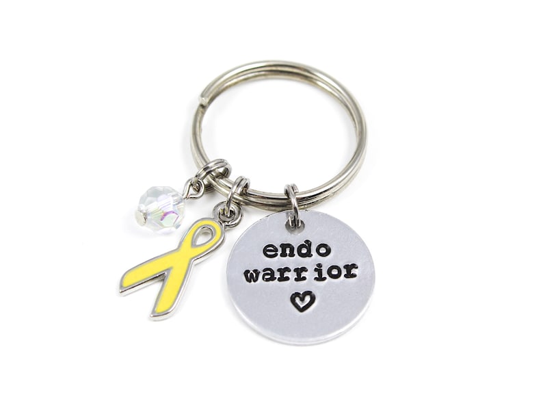 May include: Silver keychain with a yellow ribbon charm, a crystal charm, and a round silver charm with the text "endo warrior" and a heart.