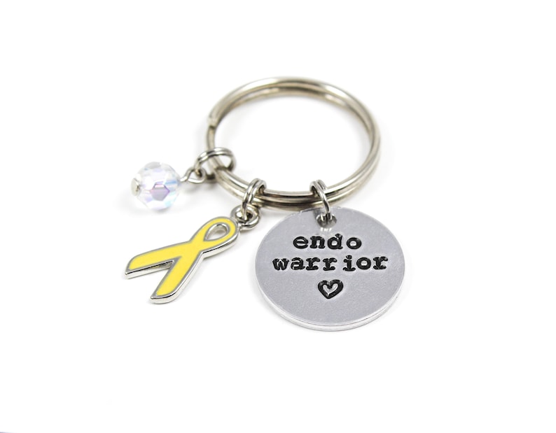 May include: A silver keychain with a yellow ribbon charm, a crystal bead, and a silver charm with the text "endo warrior" and a heart.