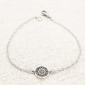May include: A silver chain bracelet with a delicate, circular pendant featuring a cutout mandala design.