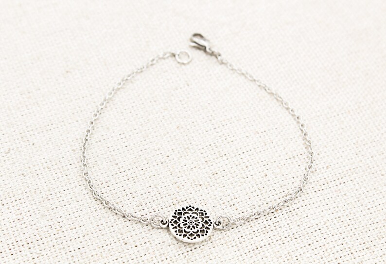 May include: A silver chain bracelet with a delicate, circular pendant featuring a cutout mandala design.