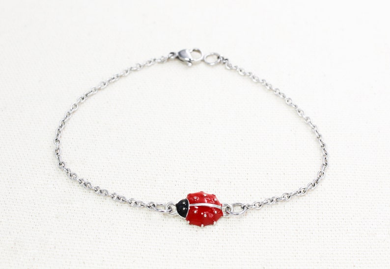 Puede incluir: Un brazalete de cadena de plata con un dije de mariquita roja y negra.