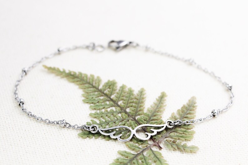 May include: A silver chain bracelet with a delicate wing charm. The bracelet has small beads along the chain.