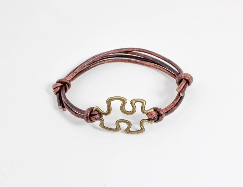 May include: A brown leather bracelet with a gold-toned puzzle piece charm.