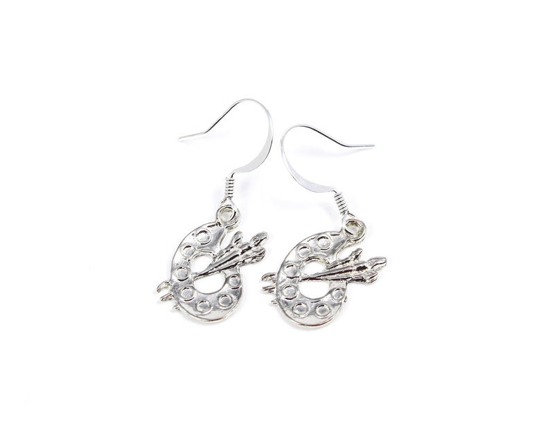 May include: Silver dangle earrings featuring a small paint palette with a paintbrush.