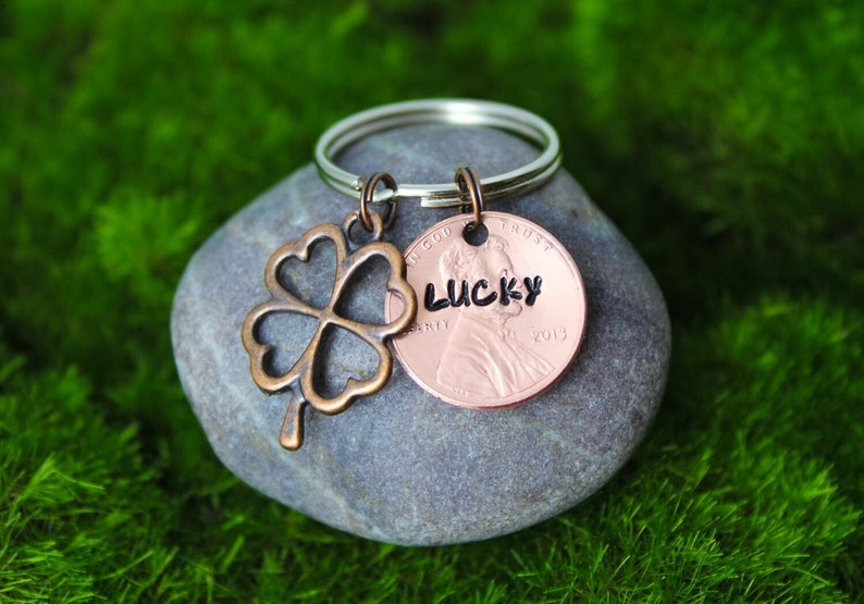 May include: A silver key chain with a copper penny charm that says "LUCKY" and a four-leaf clover charm.