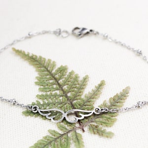 May include: A silver chain bracelet with a delicate wing charm. The bracelet has small silver beads along the chain.