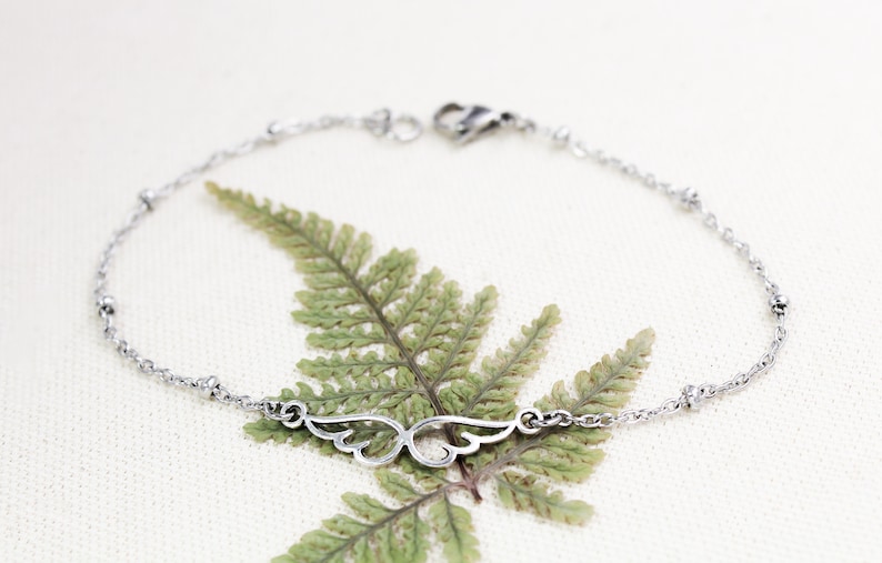 May include: A silver chain bracelet with a delicate wing charm. The bracelet has small silver beads along the chain.