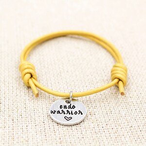 May include: Yellow leather bracelet with a silver charm that reads "endo warrior" with a small heart.