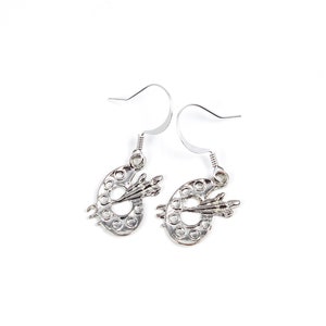May include: Silver earrings shaped like a painter's palette with a paintbrush on top.