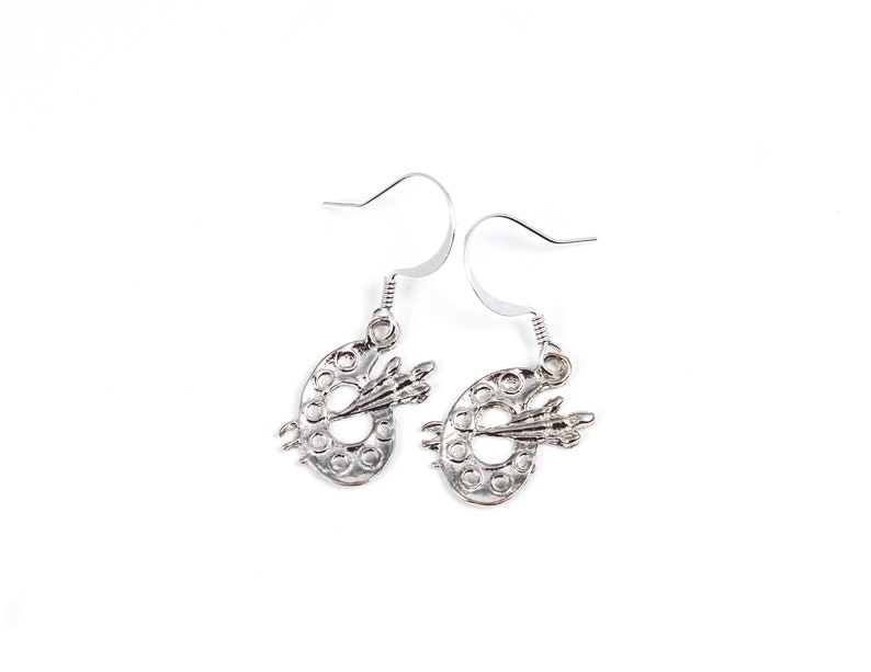 May include: Silver earrings shaped like a painter's palette with a paintbrush on top.