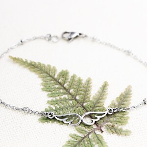 May include: A silver chain bracelet with a delicate wing charm. The bracelet has small beads along the chain.