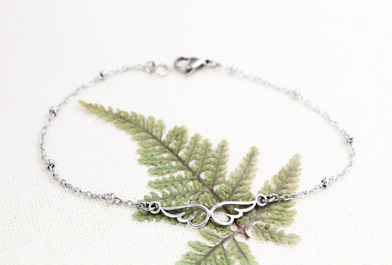 May include: A silver chain bracelet with a delicate wing charm. The bracelet has small beads along the chain.
