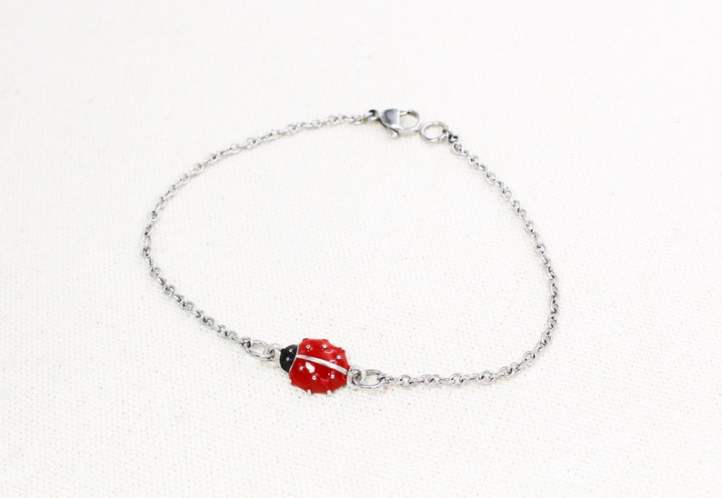Puede incluir: Un brazalete de cadena de plata con un dije de mariquita roja.