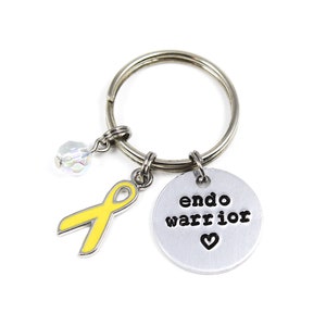 May include: A silver keychain with a yellow ribbon charm, a crystal charm, and a silver charm with the text "endo warrior" and a heart.