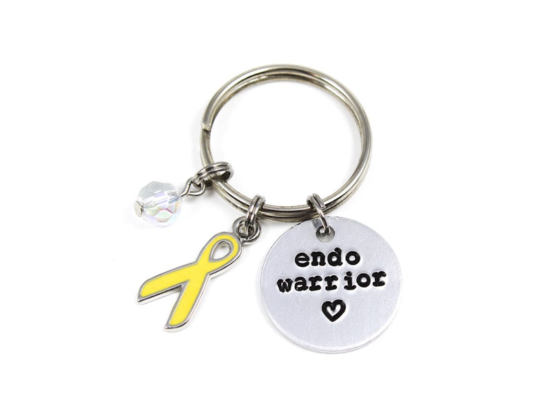 May include: A silver keychain with a yellow ribbon charm, a crystal charm, and a silver charm with the text "endo warrior" and a heart.