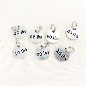 May include: Seven silver metal weight markers with different weight labels in pounds: 10 lbs, 15 lbs, 20 lbs, 25 lbs, 30 lbs, 40 lbs, and 50 lbs.