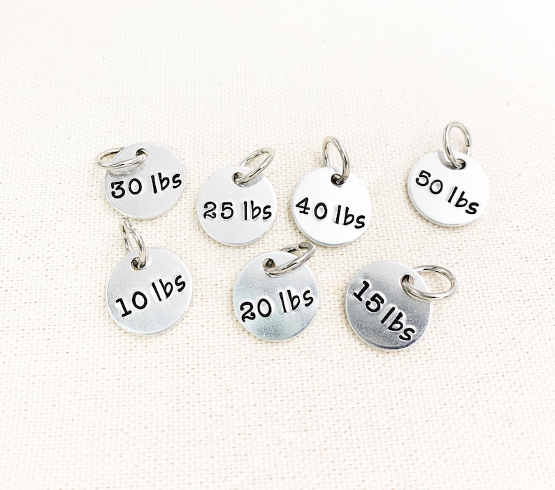 May include: Seven silver metal weight markers with different weight labels in pounds: 10 lbs, 15 lbs, 20 lbs, 25 lbs, 30 lbs, 40 lbs, and 50 lbs.