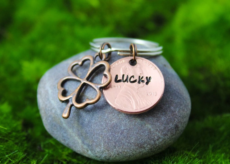 May include: A copper penny keychain with a four-leaf clover charm and the word "LUCKY" engraved on the coin. The coin is dated 2019.