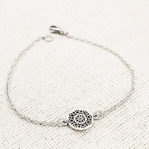 May include: A silver chain bracelet with a delicate, circular pendant featuring a cutout design.
