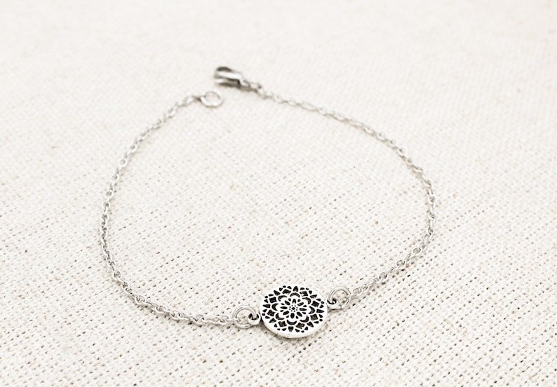 May include: A silver chain bracelet with a delicate, circular pendant featuring a cutout design.