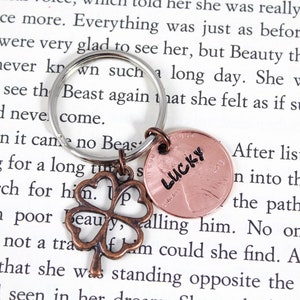 May include: A silver key chain with a four-leaf clover charm and a copper penny with the word "LUCKY" inscribed on it.