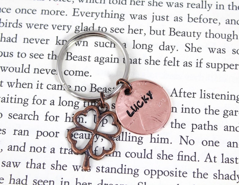 May include: A silver key chain with a four-leaf clover charm and a copper penny with the word "LUCKY" inscribed on it.