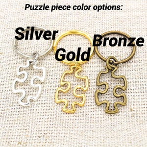 May include: Three puzzle piece keychains in silver, gold, and bronze. The keychains are attached to key rings.