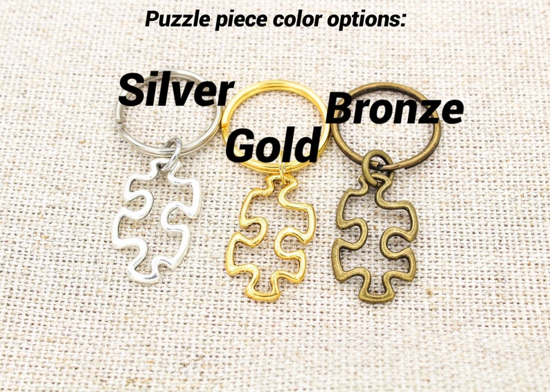 May include: Three puzzle piece keychains in silver, gold, and bronze. The keychains are attached to key rings.