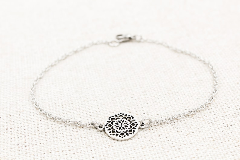 May include: A silver chain bracelet with a delicate, circular pendant featuring a cutout mandala design.