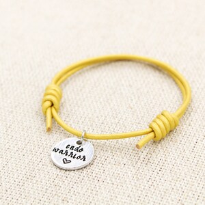 May include: A yellow leather bracelet with a silver charm that says "endo warrior" with a heart.