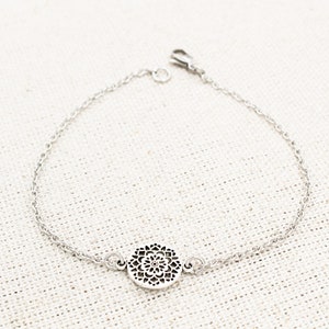 May include: A silver chain bracelet with a delicate, circular pendant featuring a cutout mandala design.