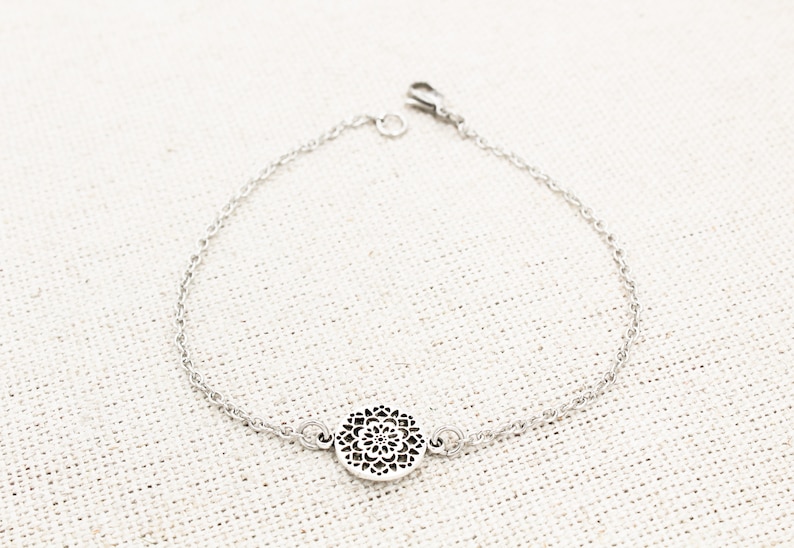 May include: A silver chain bracelet with a delicate, circular pendant featuring a cutout mandala design.