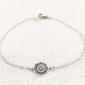 May include: A silver chain bracelet with a delicate, circular pendant featuring a detailed floral design.