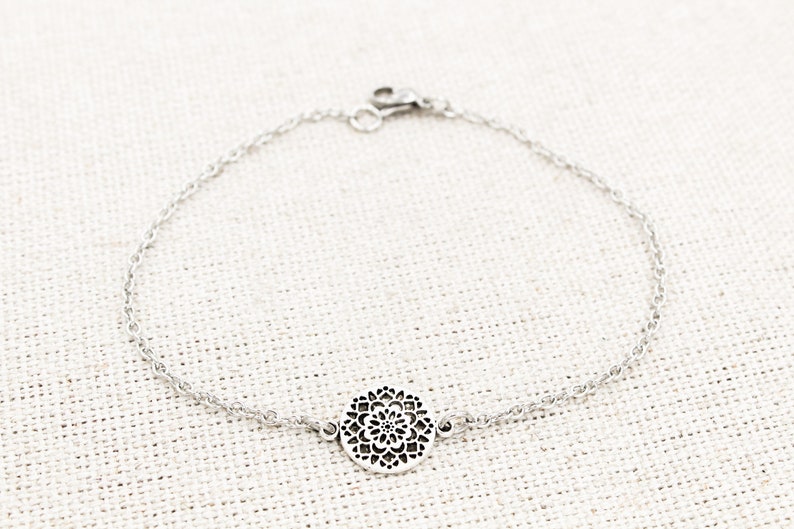 May include: A silver chain bracelet with a delicate, circular pendant featuring a detailed floral design.