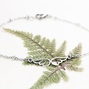 May include: A silver chain bracelet with a delicate wing charm. The bracelet has small silver beads along the chain.