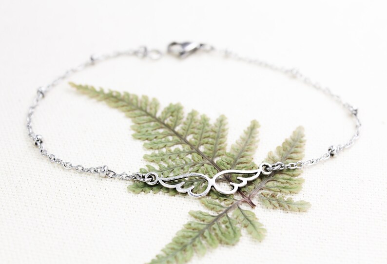 May include: A silver chain bracelet with a delicate wing charm. The bracelet has small silver beads along the chain.