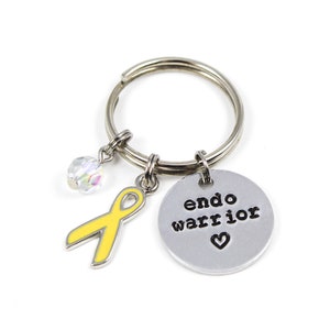 May include: A silver keychain with a yellow ribbon charm, a crystal charm, and a silver charm with the text "endo warrior" and a heart.