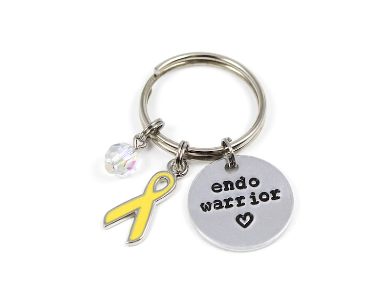 May include: A silver keychain with a yellow ribbon charm, a crystal charm, and a silver charm with the text "endo warrior" and a heart.