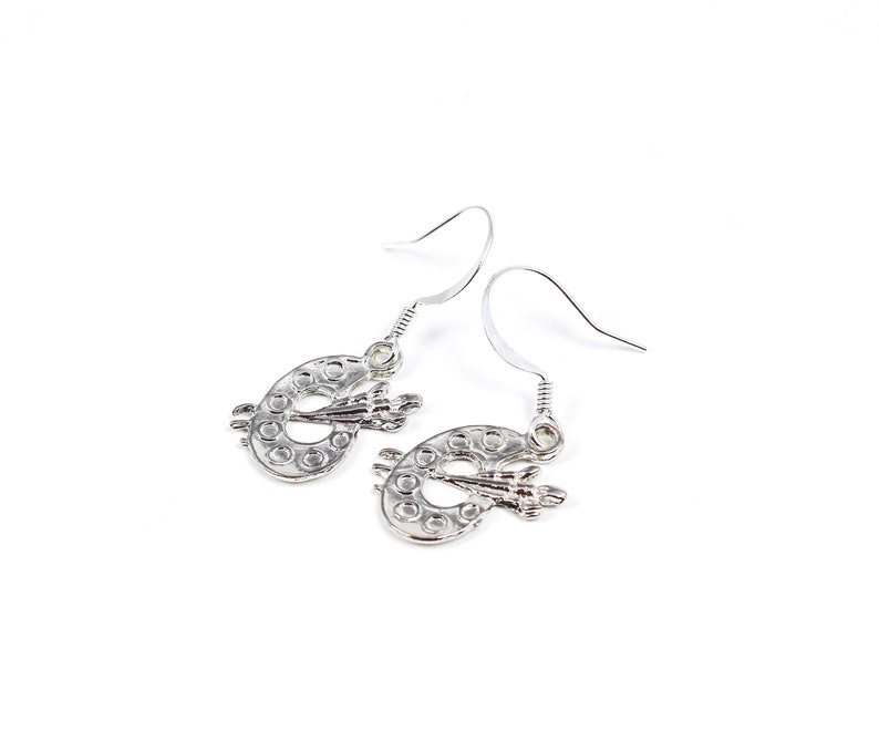 May include: Silver earrings shaped like a paint palette with a paintbrush on top.