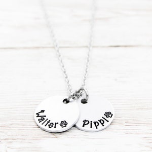 May include: Silver necklace with two round pendants. The pendants are engraved with the names "Walter" and "Pippi" and a paw print.