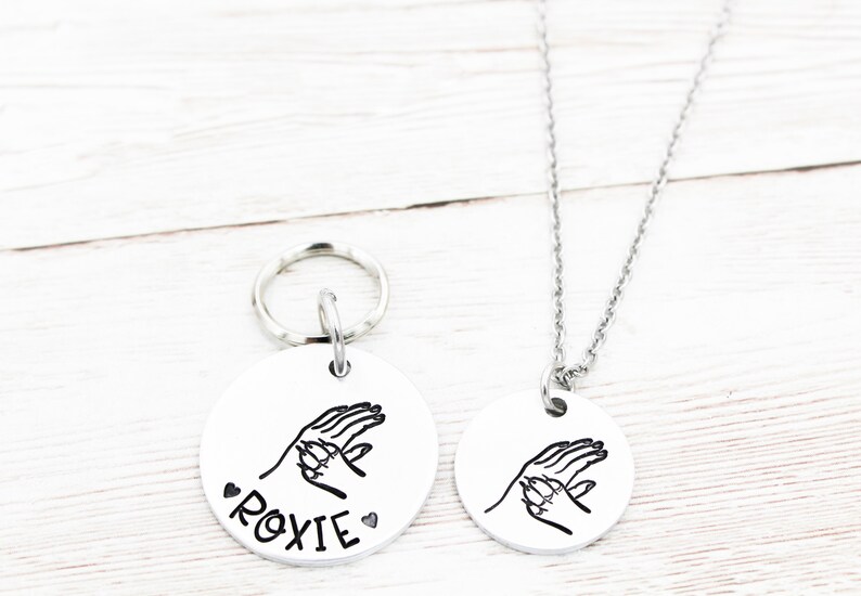 May include: Silver dog tag necklace and keyring set with a paw print design and the name "ROXIE" on the tag.
