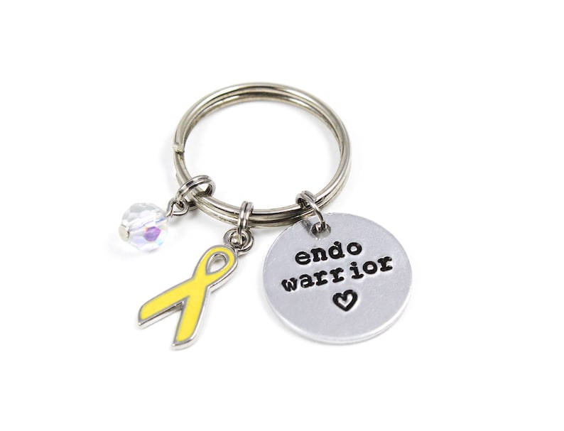 May include: A silver keychain with a yellow ribbon charm, a crystal charm, and a silver charm with the text "endo warrior" and a heart.
