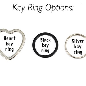 Puede incluir: Tres opciones de llavero: un llavero de coraz&oacute;n plateado, un llavero circular negro y un llavero circular plateado. Cada llavero tiene las palabras "key ring" impresas.