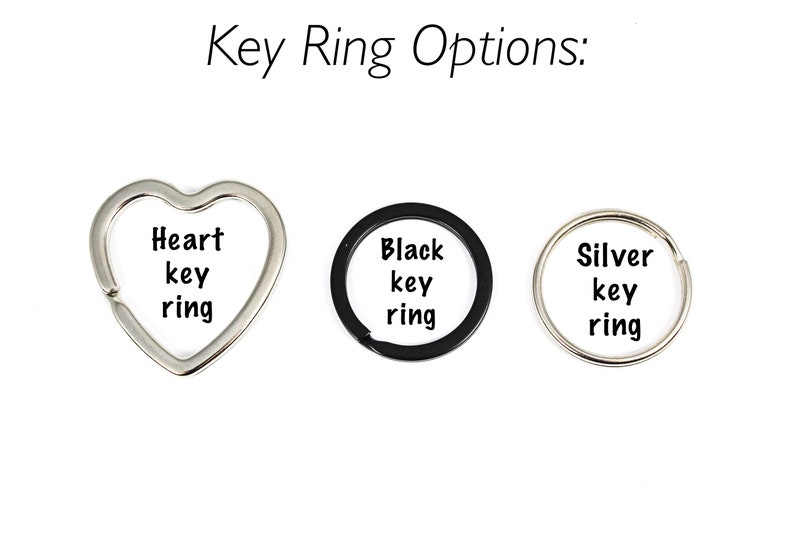 Puede incluir: Tres opciones de llavero: un llavero de coraz&oacute;n plateado, un llavero circular negro y un llavero circular plateado. Cada llavero tiene las palabras "key ring" impresas.