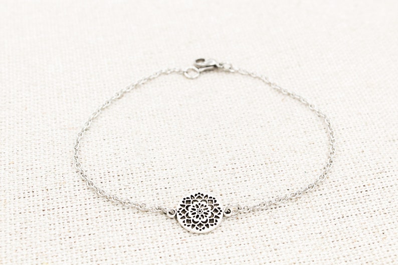 May include: A silver chain bracelet with a delicate, circular pendant featuring a detailed, intricate design.