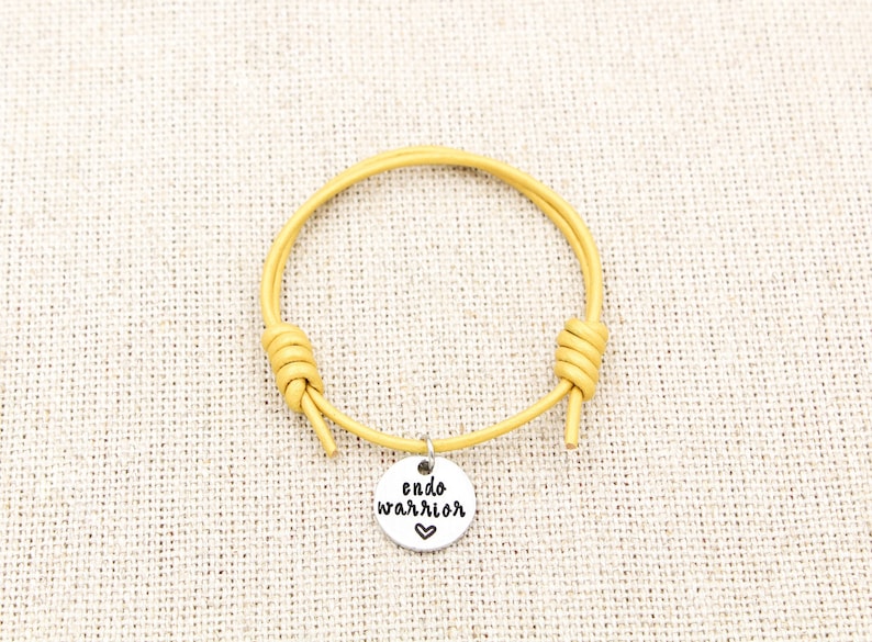 May include: A yellow leather bracelet with a silver charm that says "endo warrior" with a heart.